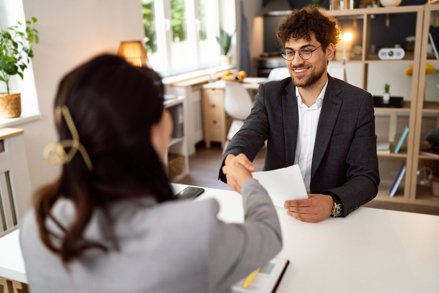 A young man wearing a business suit shakes hands with a job recruiter.