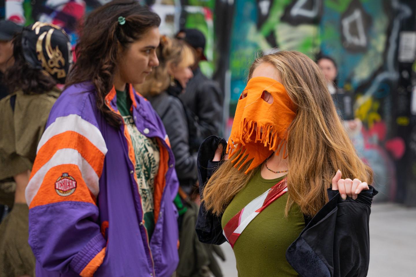 A couple protesters are standing and wearing colorful clothing and masks.