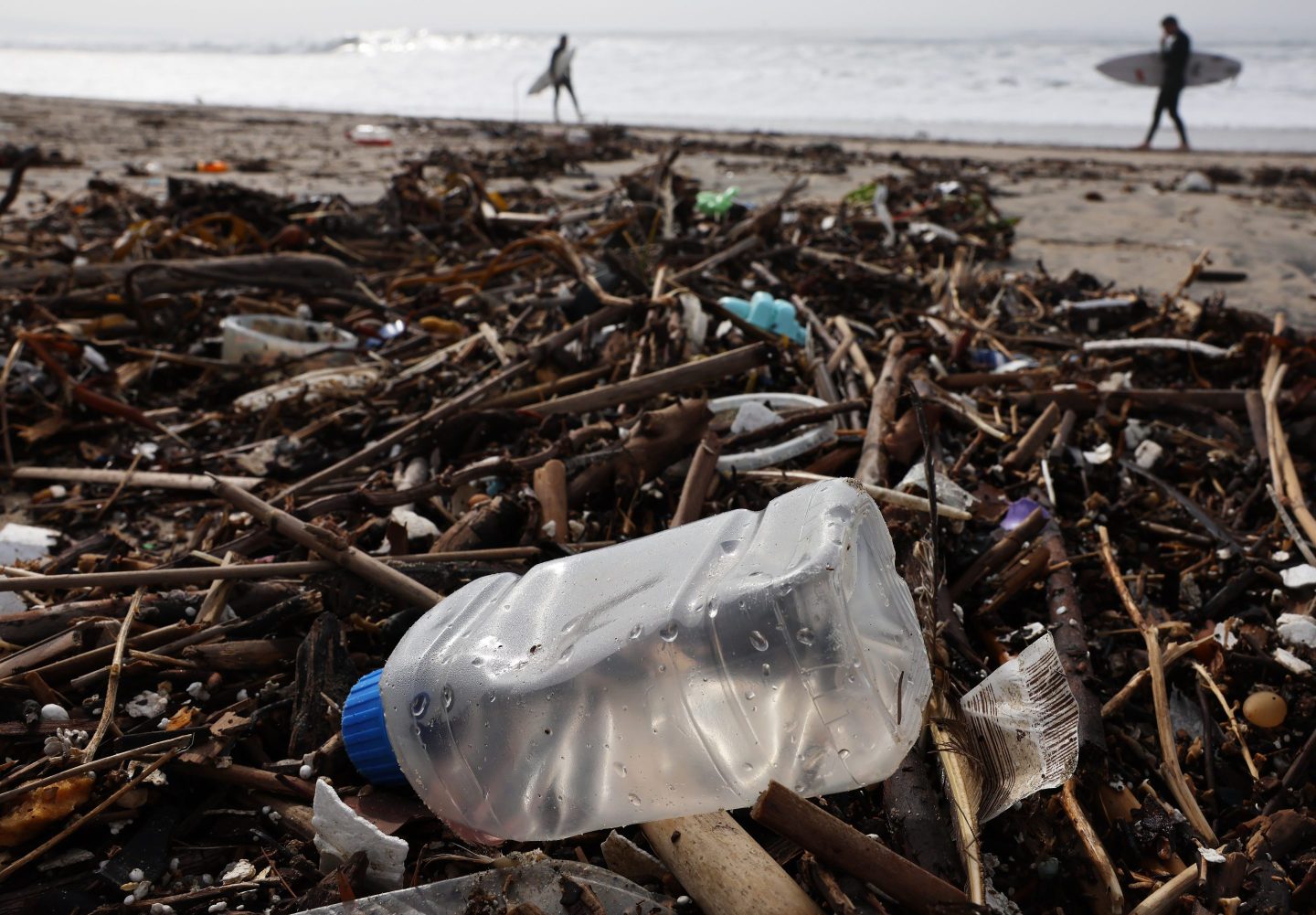 Surfers walk near debris, including a plastic bottle, in El Segundo, Calfornia.