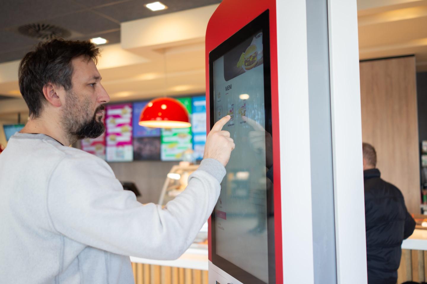 A man at a self-service kiosk uses a touch screen to place an order.
