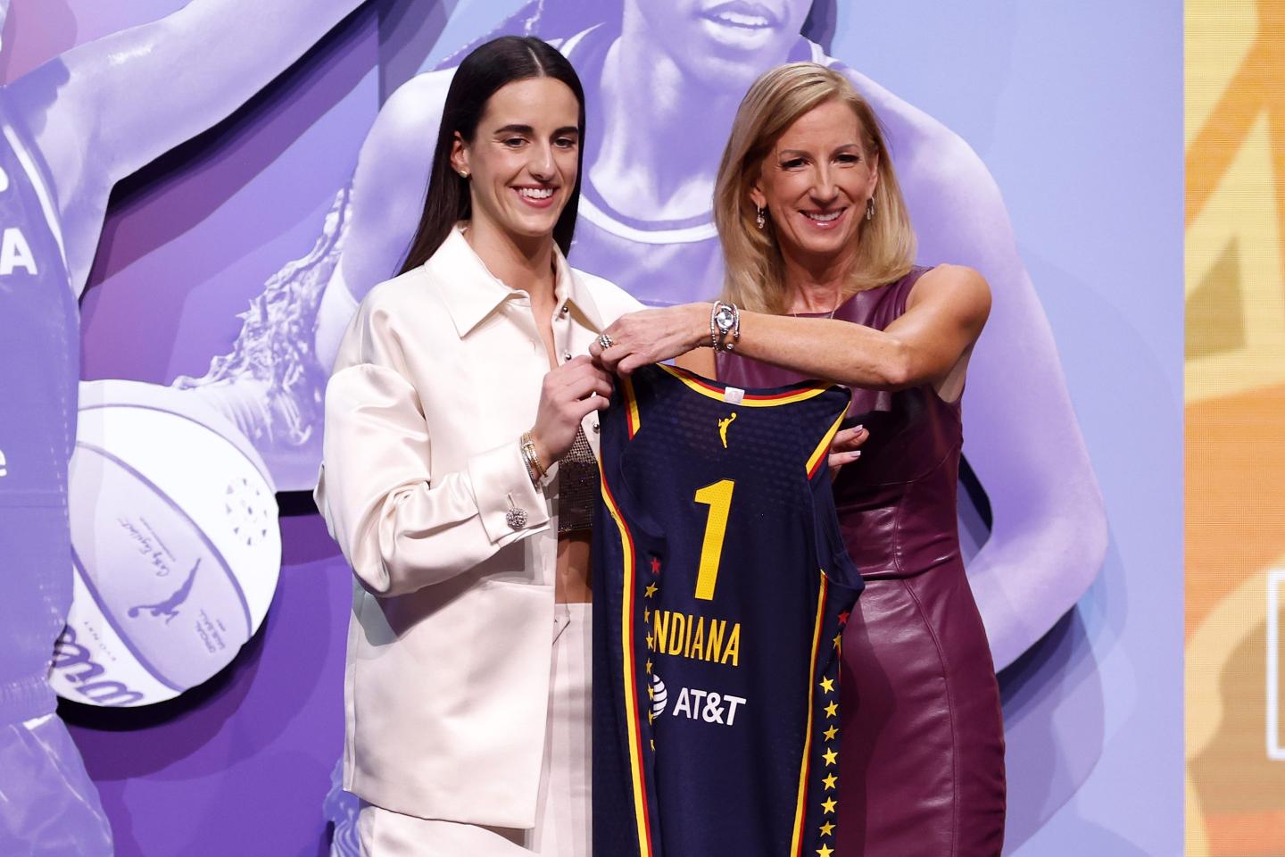 Caitlin Clark is holding up one side of an Indiana Fever jersey as WNBA Commissioner Cath Engelbert holds up the other