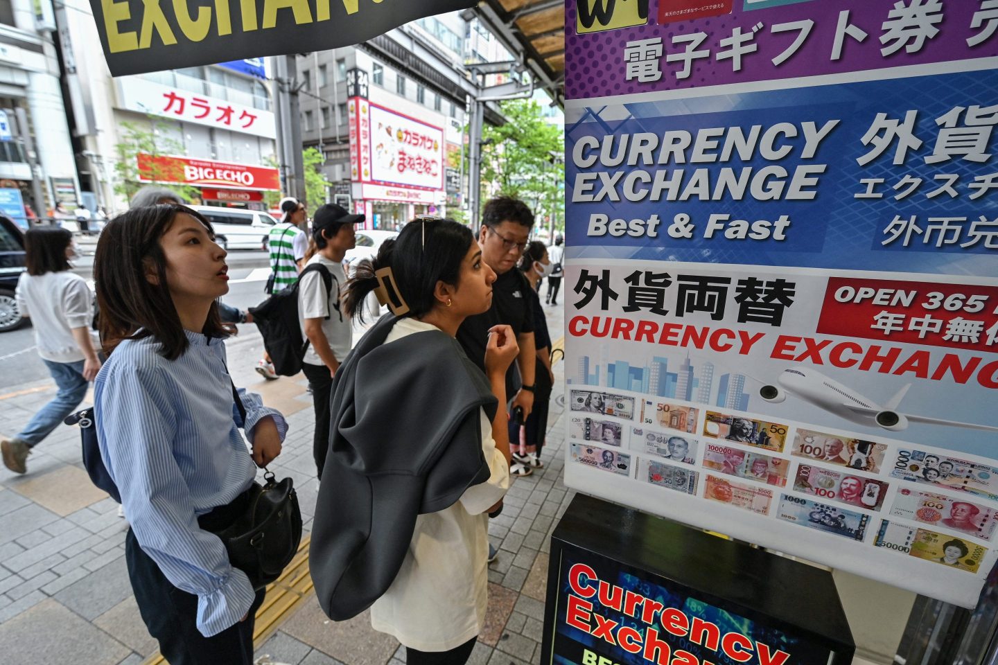 People stand outside a money changer looking at the rates of the Japanese yen against foreign currencies, along a street in central Tokyo on April 29, 2024.
