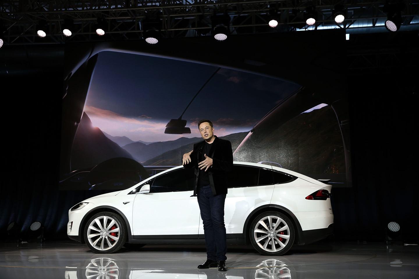 elon musk stands in front of a white car on a stage