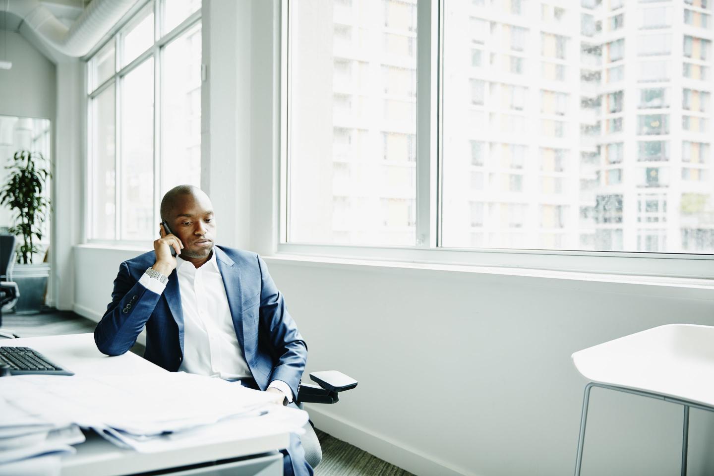 Frustrated businessman sitting at office workstation waiting while on smartphone