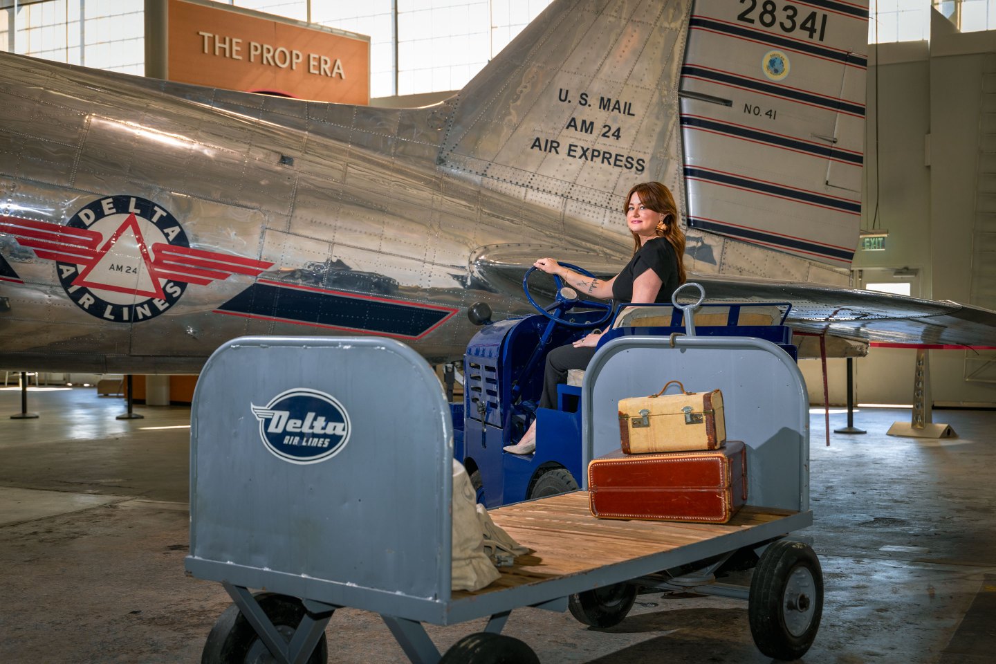 At the Delta Flight Museum, director of exhibits Nina Thomas sits in a luggage trolley alongside Delta Douglas DC-3 Ship 41, which first flew for the airline in 1941.