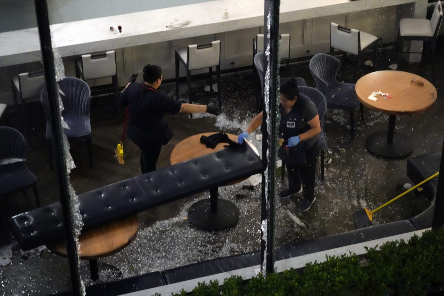 Workers clean up broken glass inside a damaged downtown restaurant after a severe thunderstorm, on May 16, 2024, in Houston.