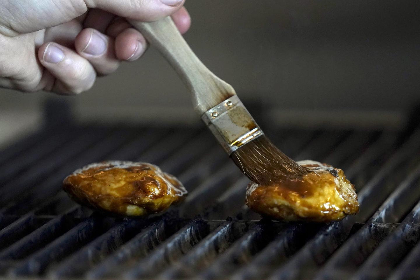 A hand brushes a piece of meat on a grill