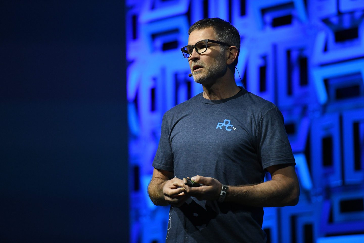 David Baszucki is standing on stage with a patterned blue screen behind him.