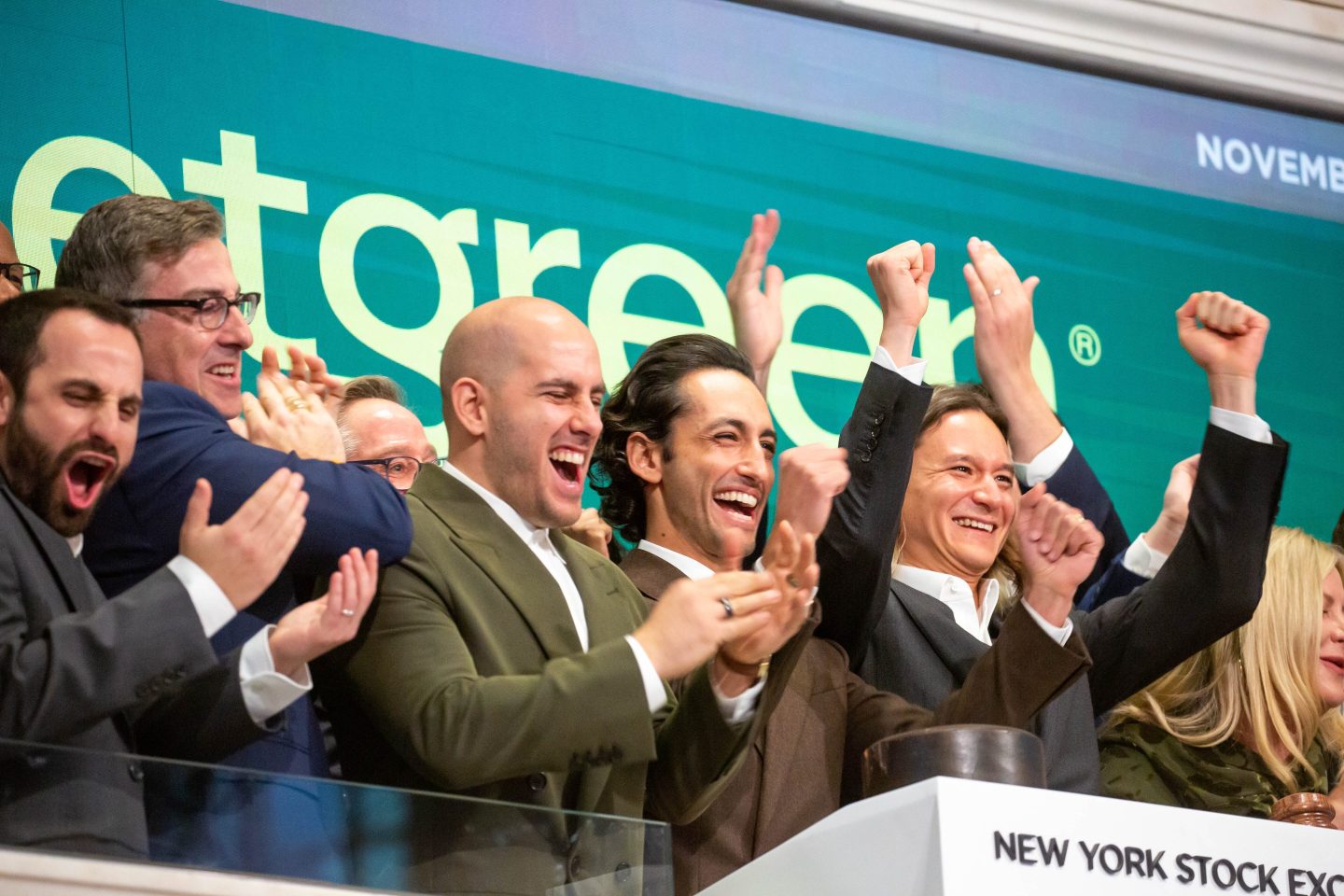 A group of men cheer on the trader floor of the NYSE in front of a green and white &quot;Sweetgreen&quot; sign.