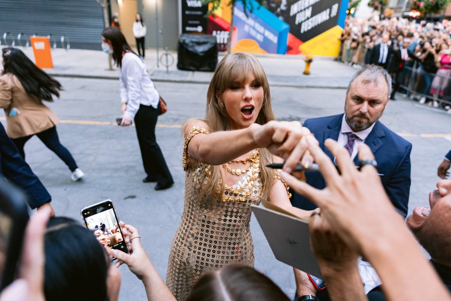 Taylor Swift is surrounded by fans as she hands back a photographed notebook and pen.