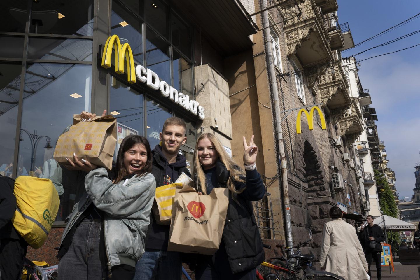 A group of three young people with paper McDonald's bags stand outside a McDonald's chain.
