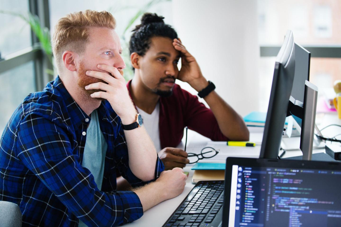 Two programmers working together on a computer code.
