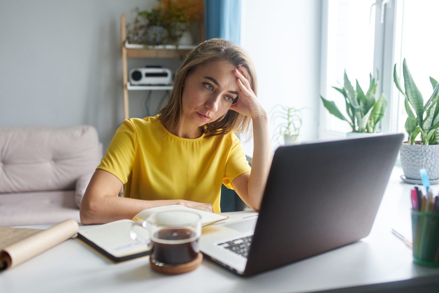 A 35-year-old woman in a bright yellow jacket is sitting in front of a laptop in emotional tension. The concept of working from home, freelance