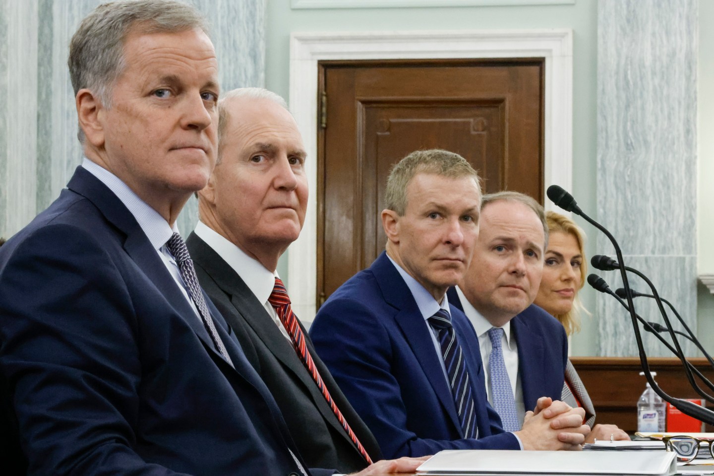 A group of men in suits, including the CEOS of United, Delta, and American Airlines sit at a long table.