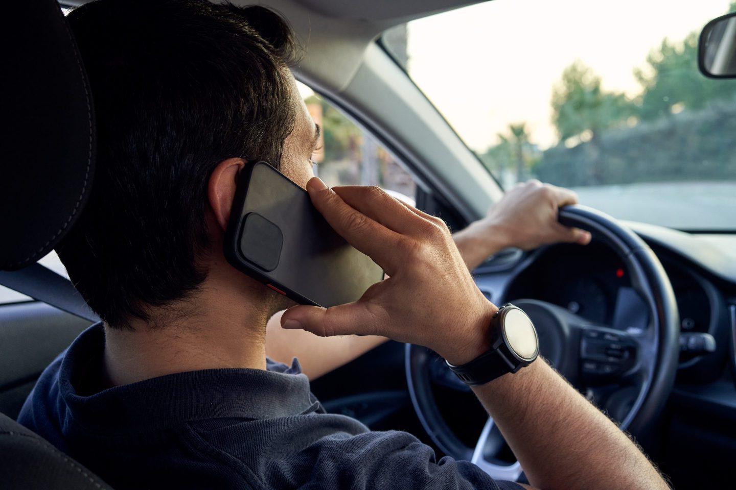 Rear view of a young unrecognizable Hispanic man talking on a smartphone while driving his car