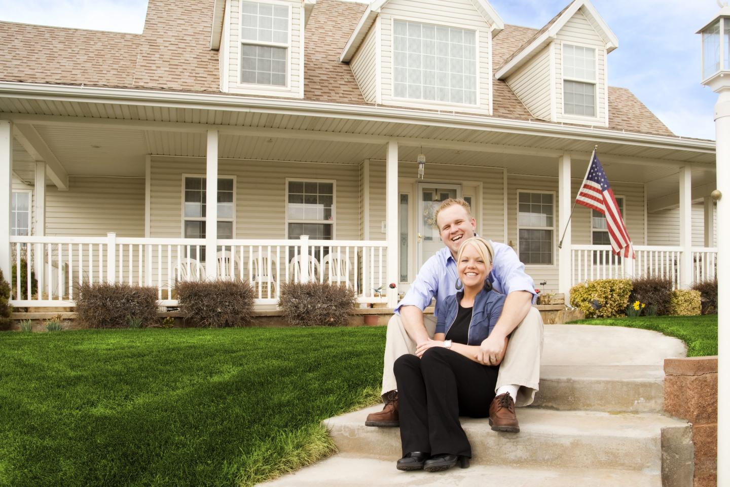 Photo of a young American couple sitting in front of their house, laughing.