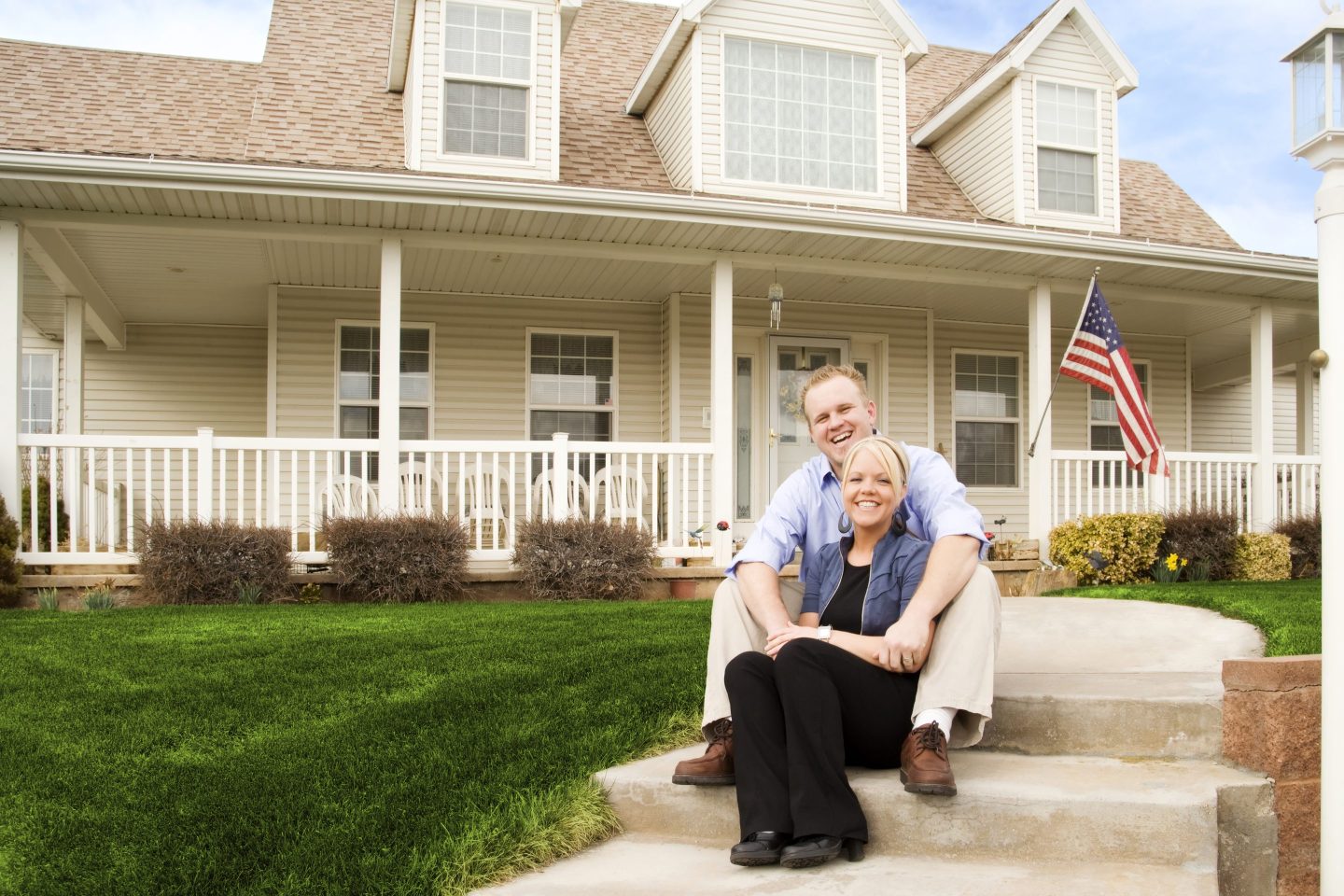 Photo of a young American couple sitting in front of their house, laughing.