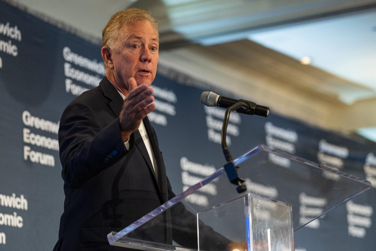 Connecticut Governor Ned Lamont standing at a podium giving a speech and raising his right arm.