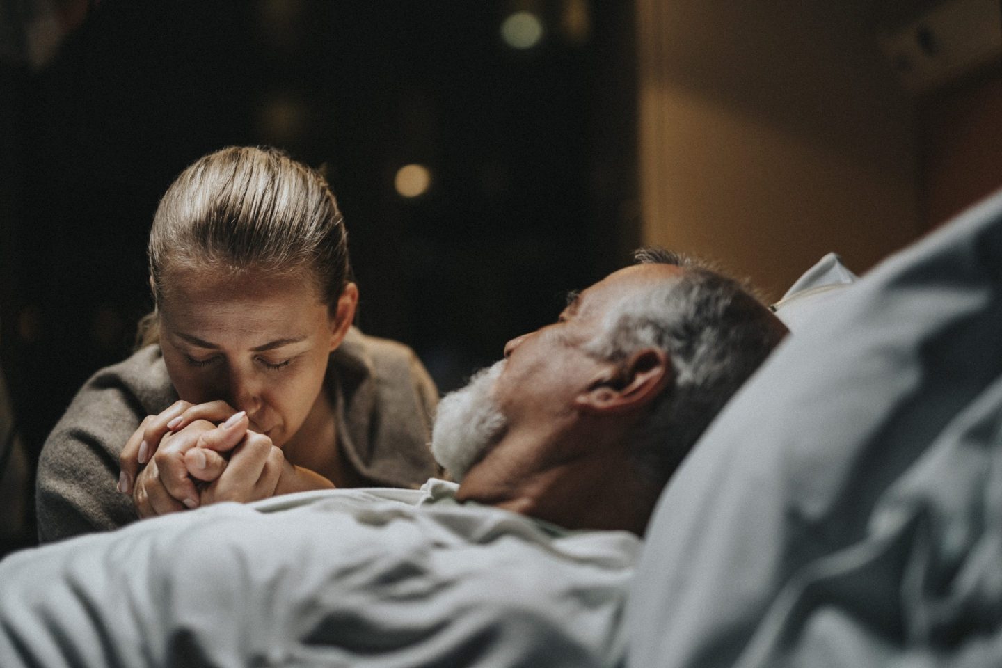 Daughter kissing on hand of father lying down in hospital