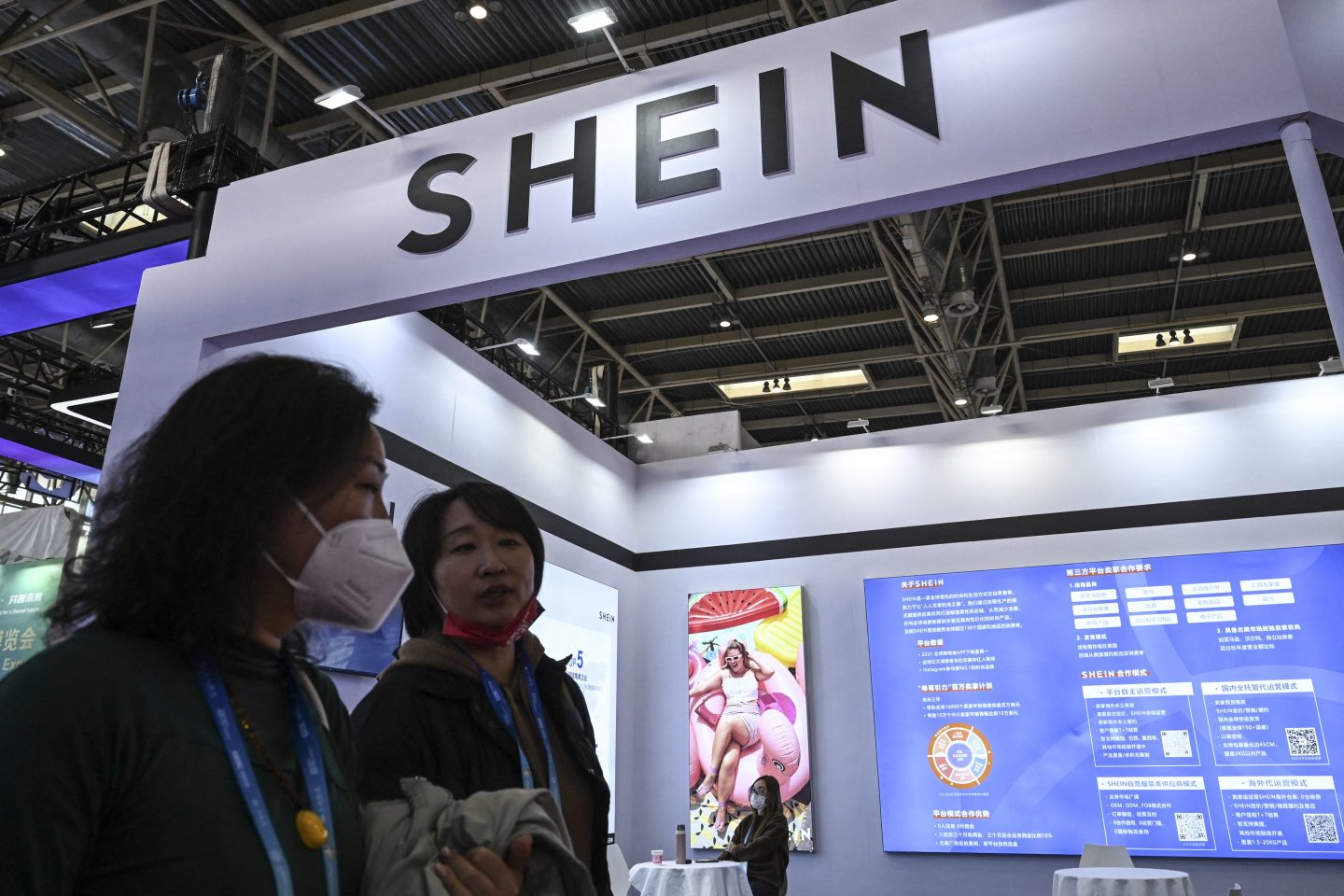 People walk past the booth of fast fashion e-commerce company SHEIN during the China International Supply Chain Expo (CISCE) in Beijing on December 1, 2023. (Photo by JADE GAO / AFP) (Photo by JADE GAO/AFP via Getty Images)