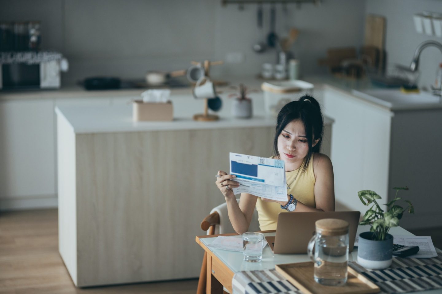 Upset woman thinking about high prices while looking at utilities, gas, electricity, rental charges, water bill due to inflation and crisis. Planning personal budget while sitting in kitchen. Weighing options on how to save money