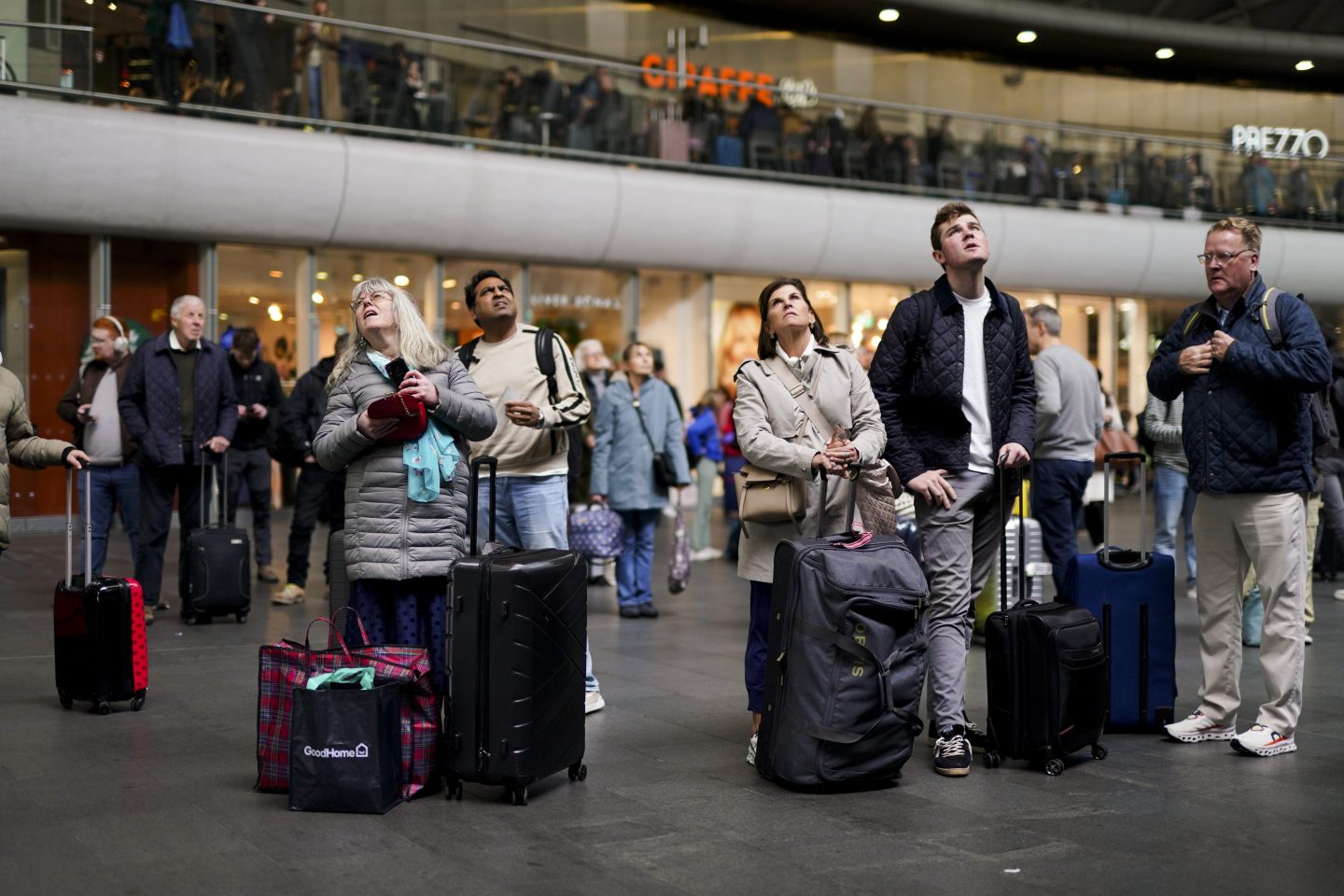 people standing at a railway station looking up at screens