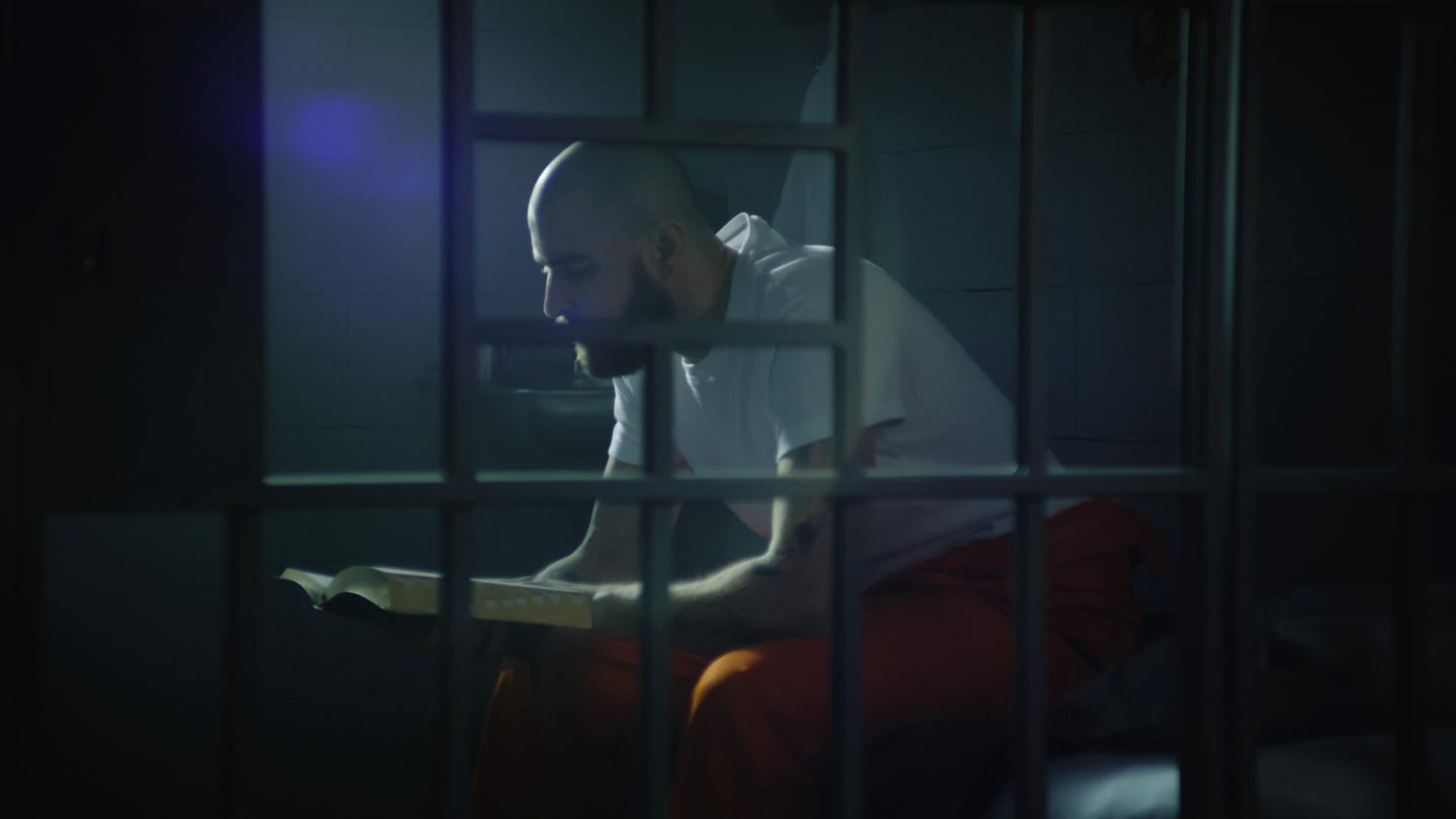 Male prisoner sits on bed in prison cell