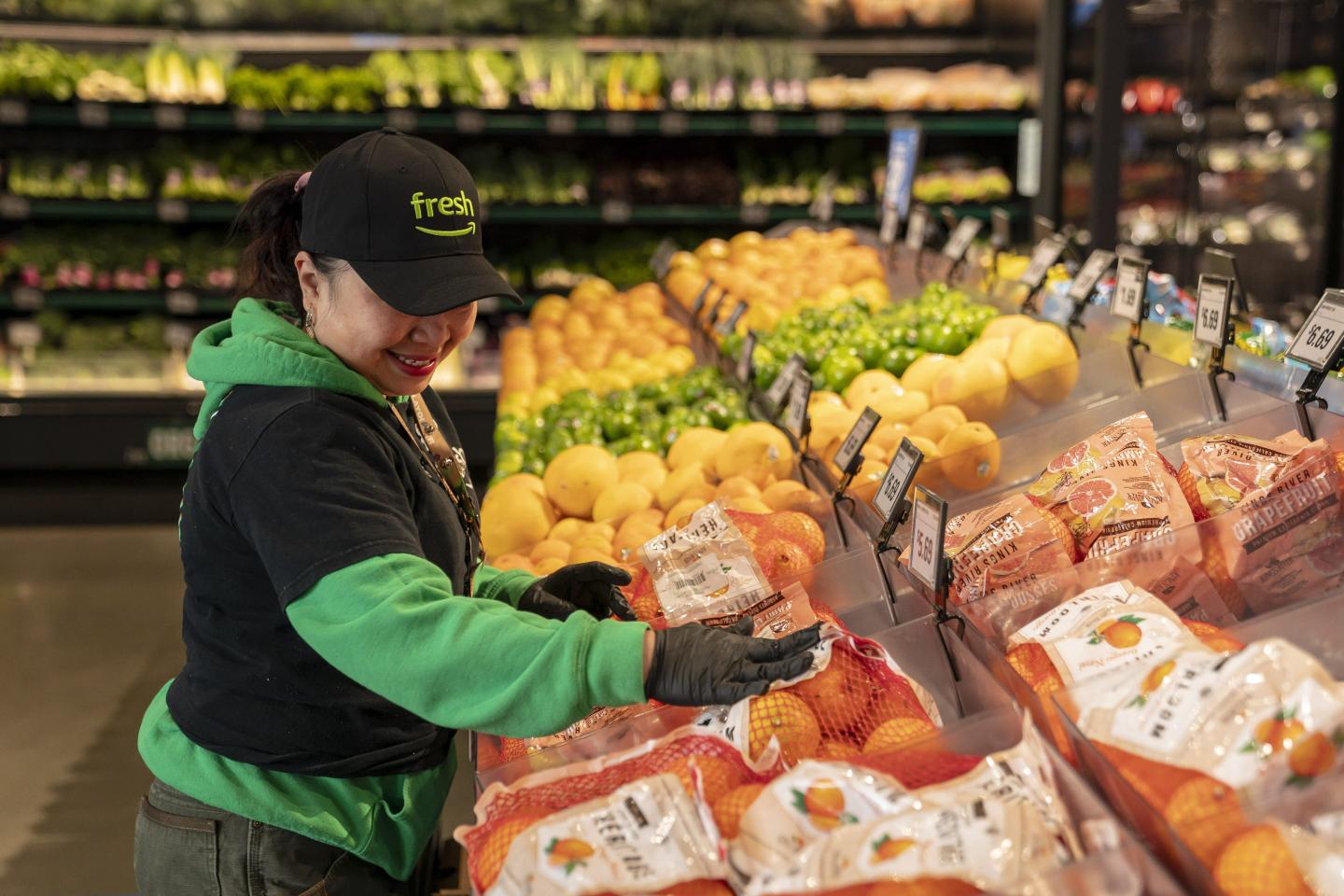 An Amazon Fresh worker restocks citrus in a store.