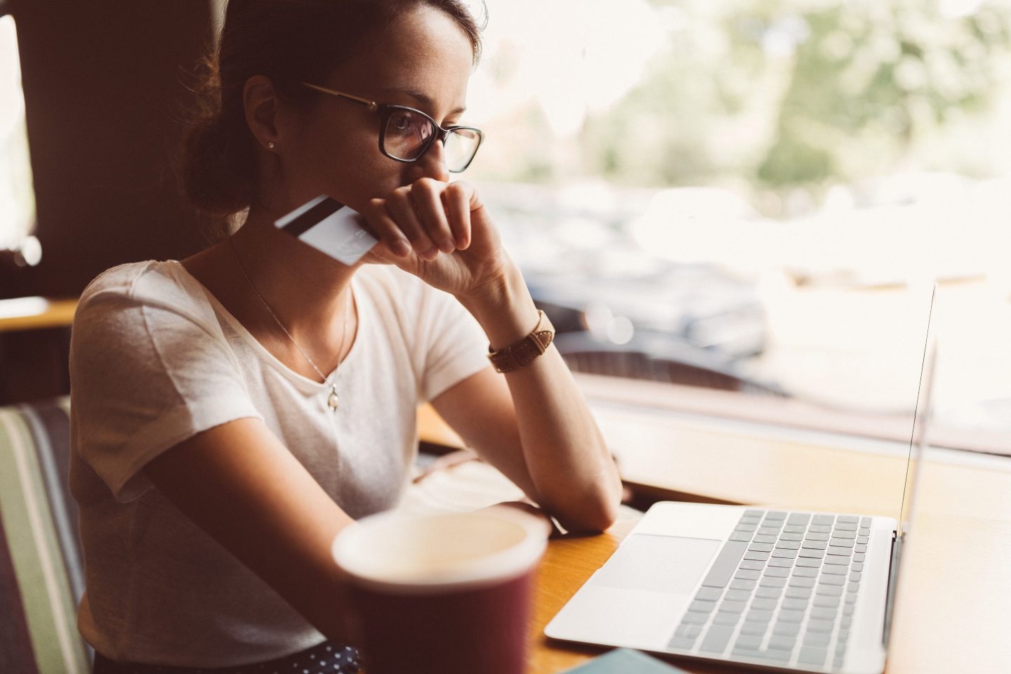 Woman sitting in front of laptop holding a credit card looking worried.