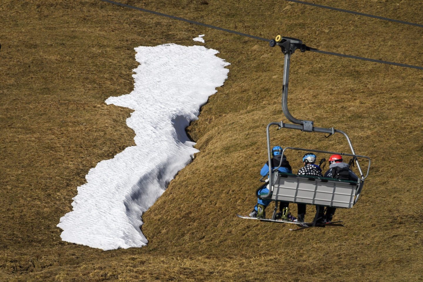 Skiers in a chairlift looking at a snowless mountain.