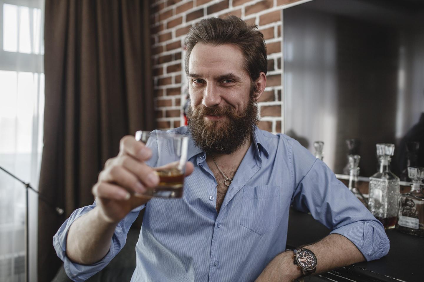 Portrait of smiling man with glass of whiskey at home.