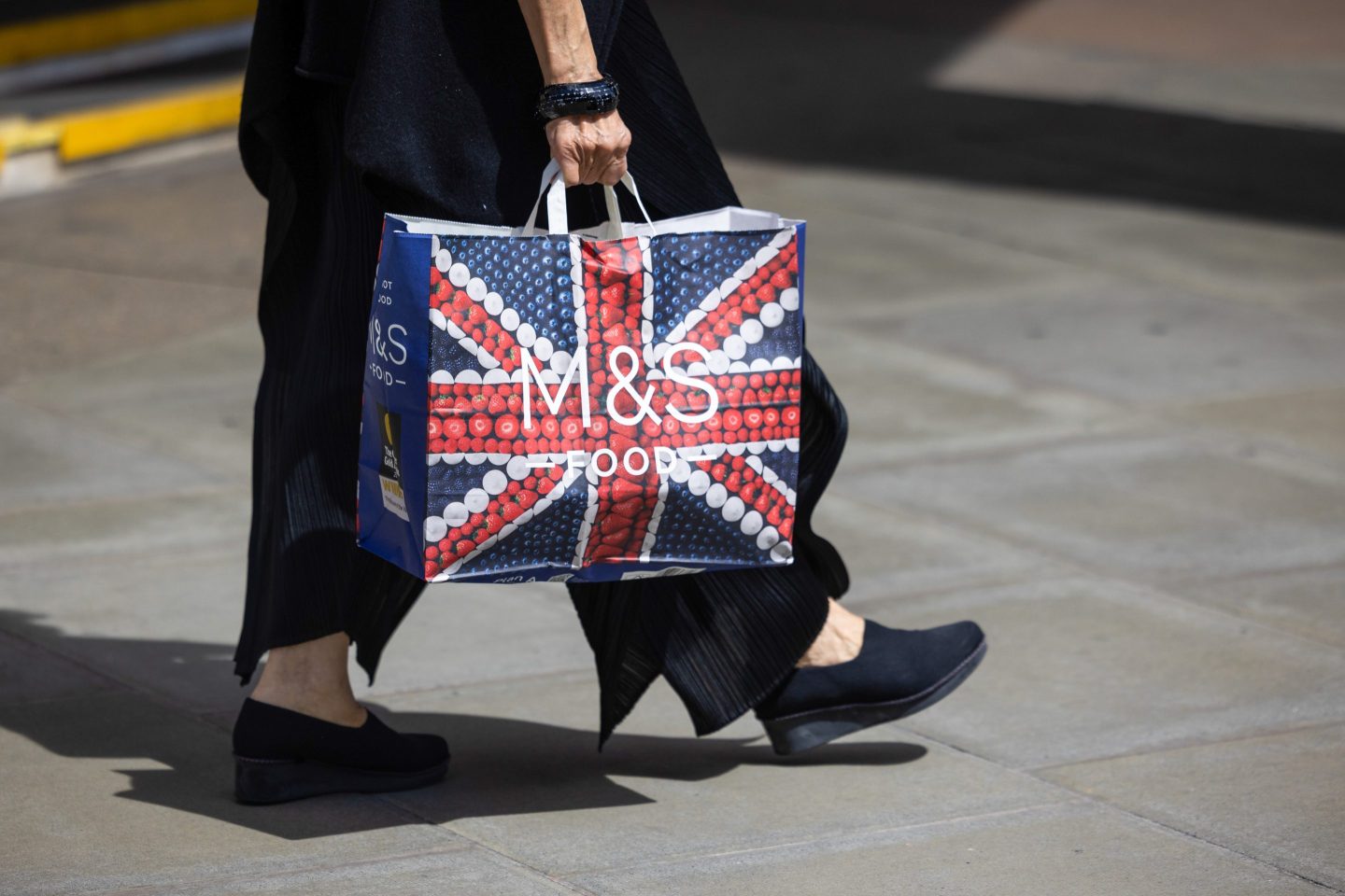 Woman carrying a Marks and Spencer shopping bag with a union jack motif.