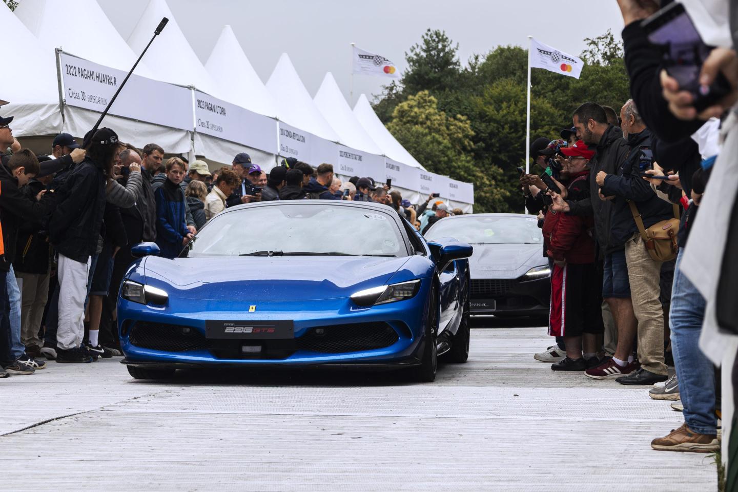 A blue Ferrari 296 GTS at the 2023 Goodwood Festival of Speed, being admired by the crowd.