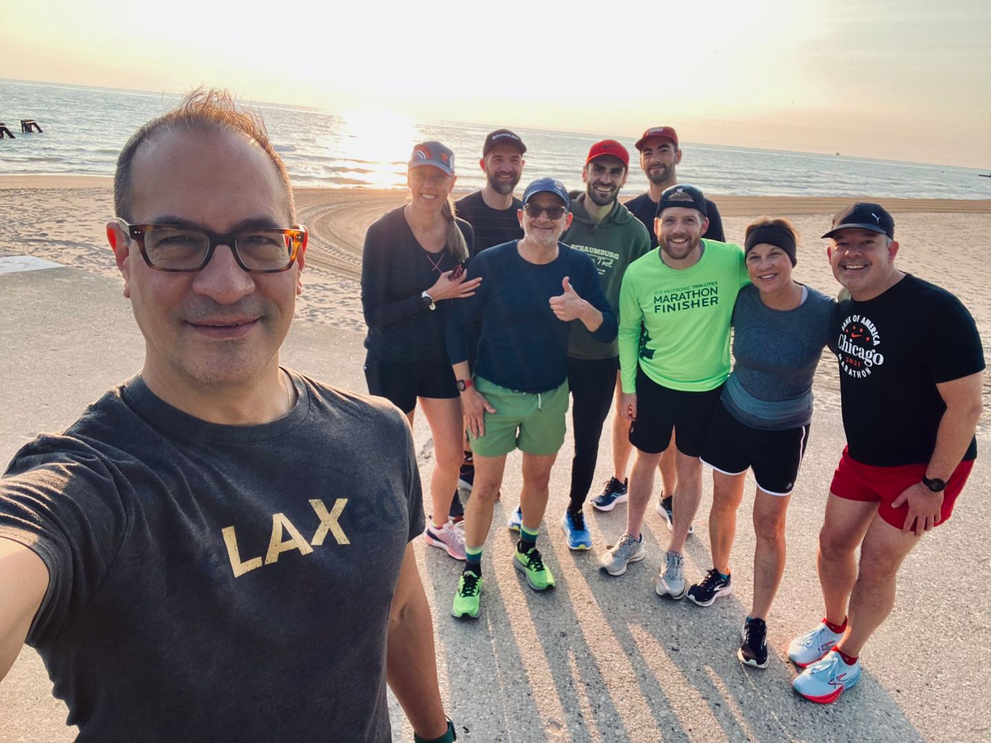A group of nine runners, one very close up in the foreground, pose on a beach.