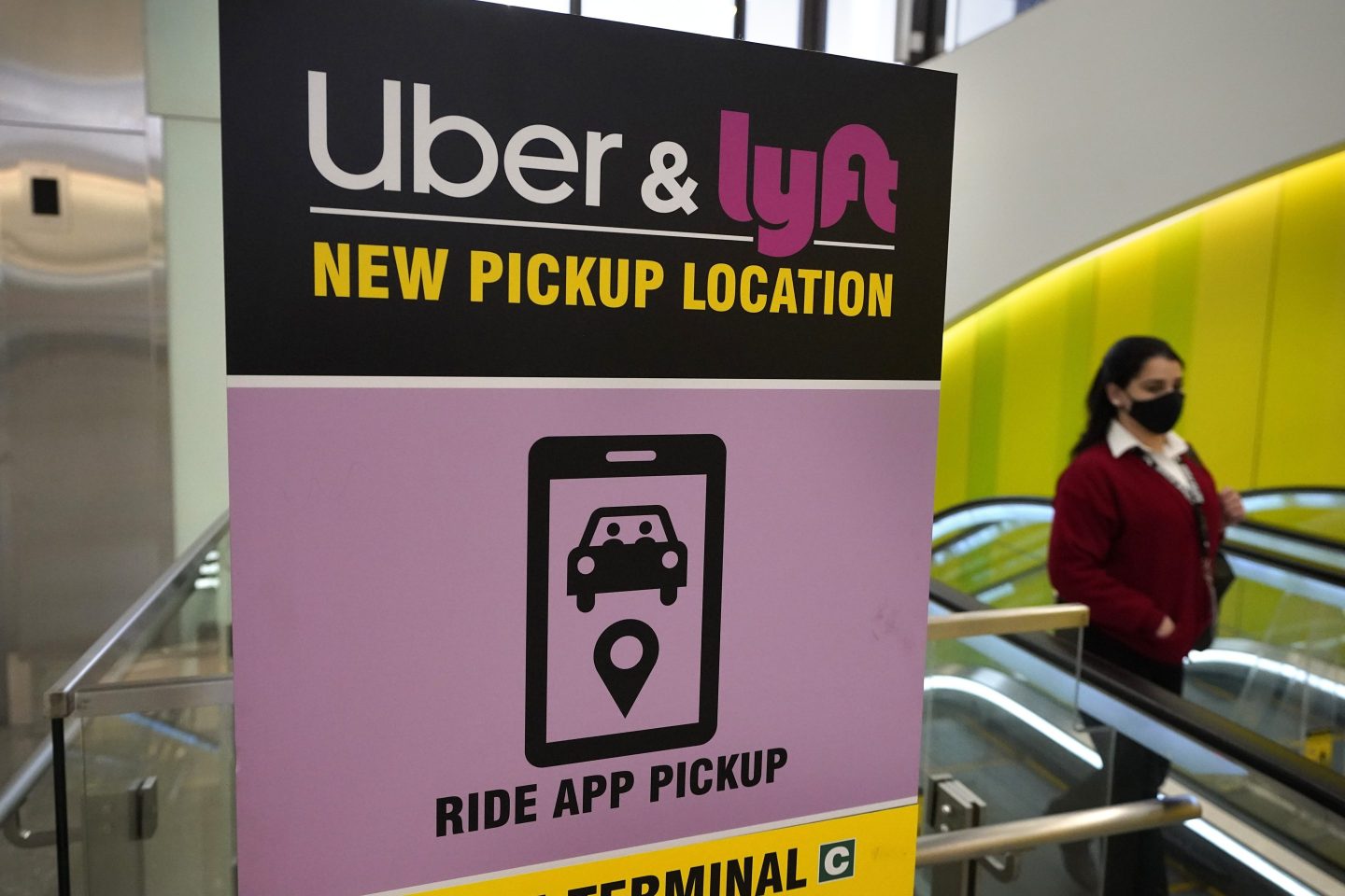 A passerby walks past a sign offering directions to an Uber and Lyft ride pickup location at an airport, Feb. 9, 2021, in Boston.