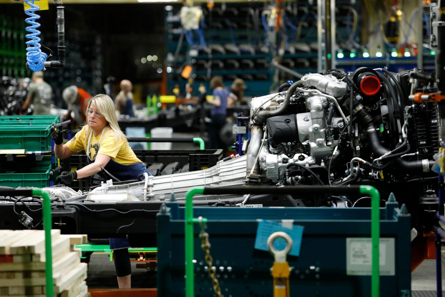 A woman with blond hair and a yellow shirt. She's a line worker working on a chassis of a pick up truck.