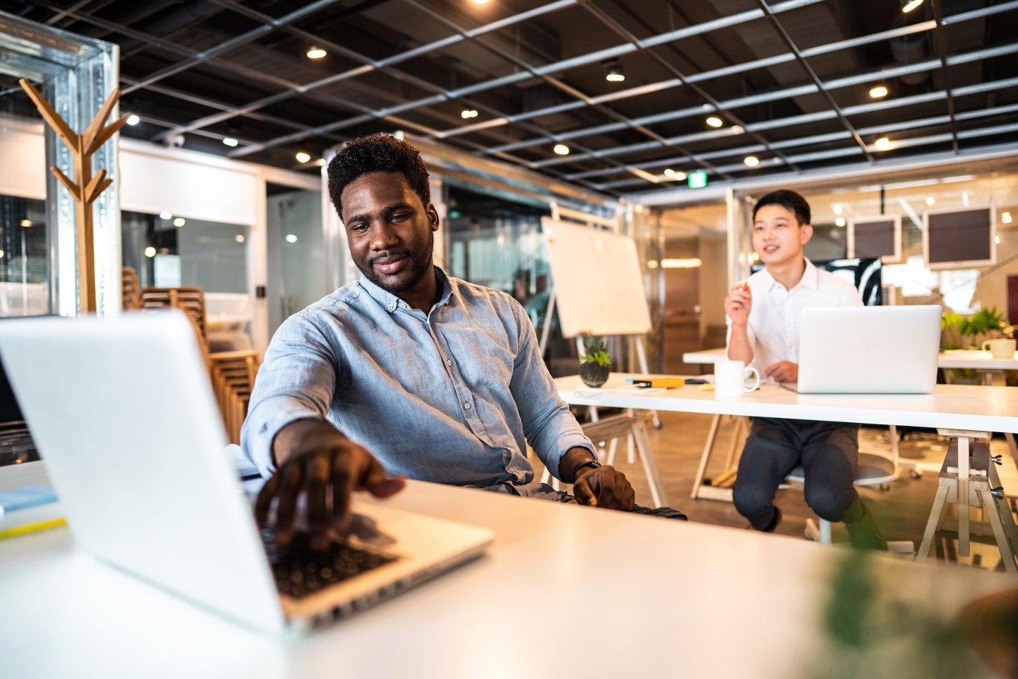 Handsome Haitian male entrepreneur sitting in modern office space, looking at laptop.