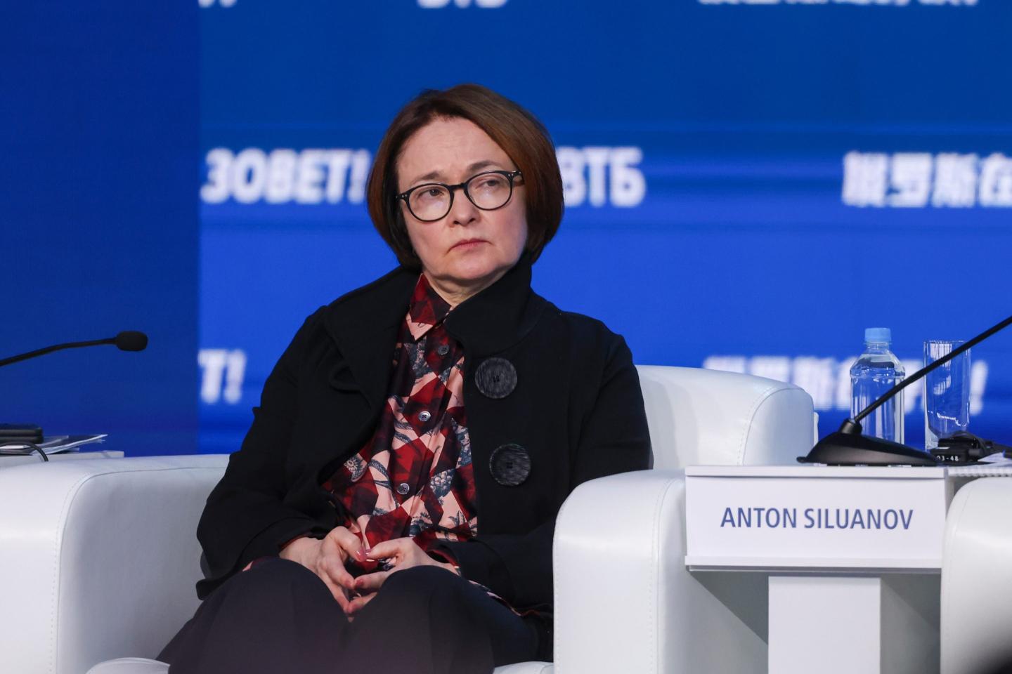 Elvira Nabiullina sits, listening with a neutral expression during a panel session at an event.