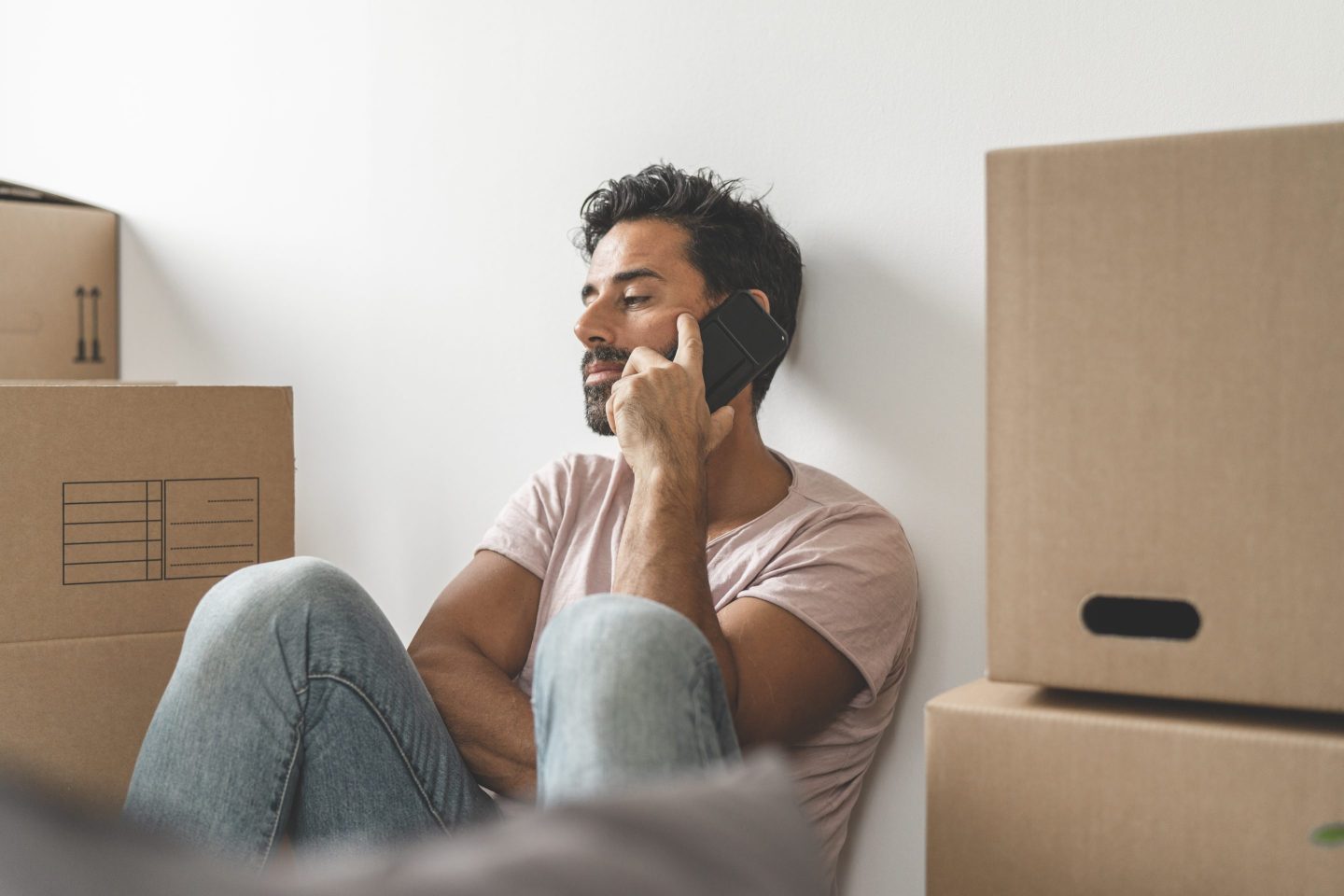 Man is sitting on the floor with his phone surrounded by moving boxes.