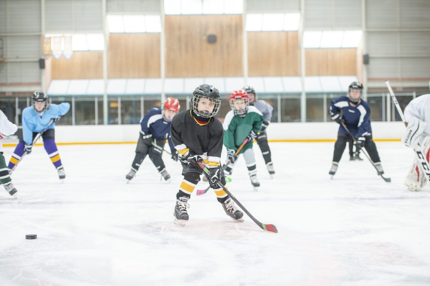 A group of kids in full hockey gear skate down the rink.