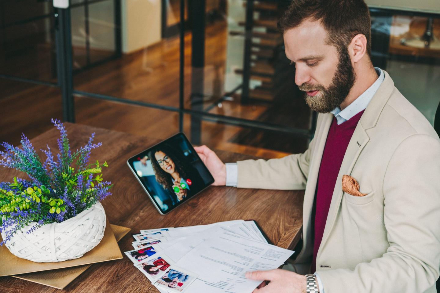 A recruiter in an office speaks to a candidate during a virtual interview while looking over a stack of résumés.