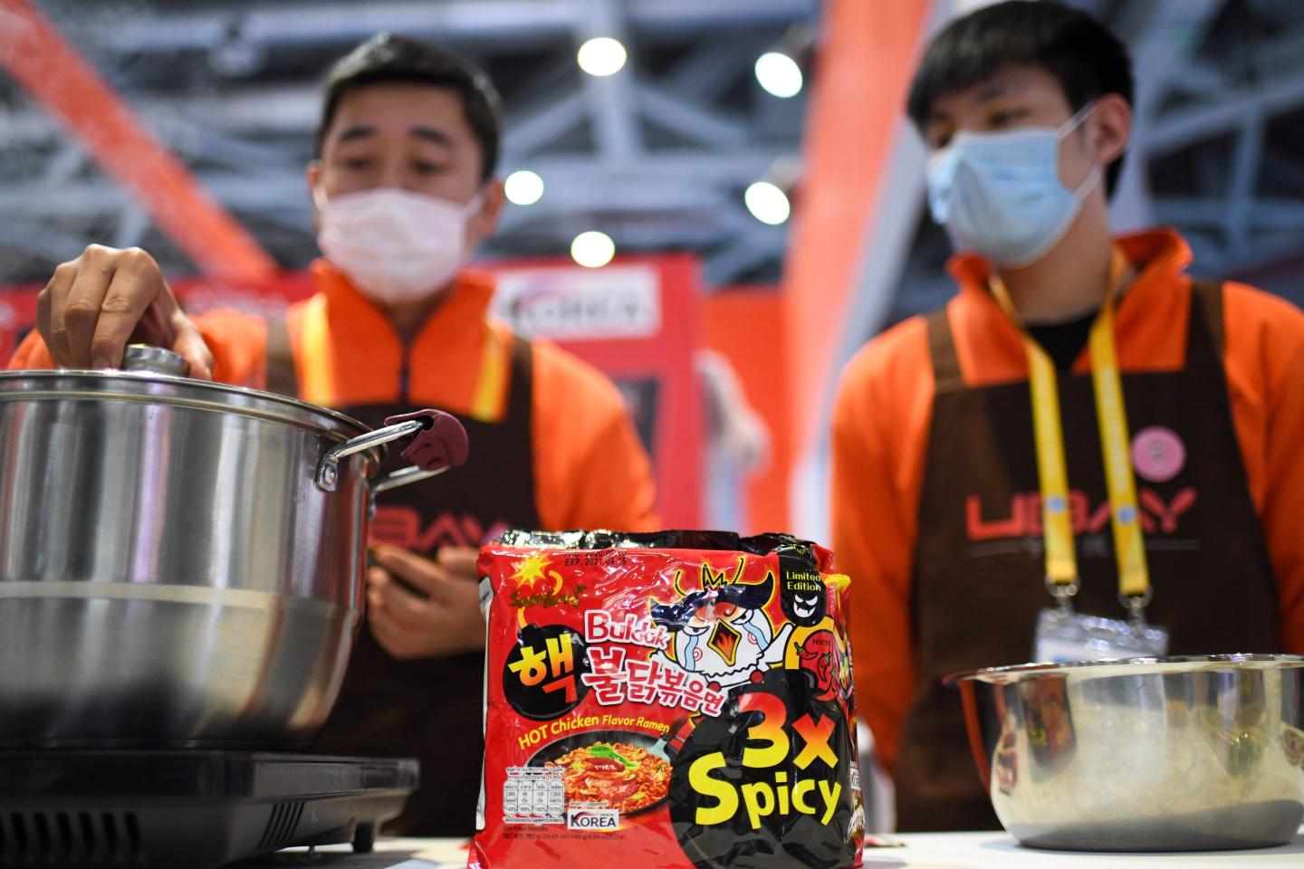 Two men cook Buldak instant ramen in large metal pots