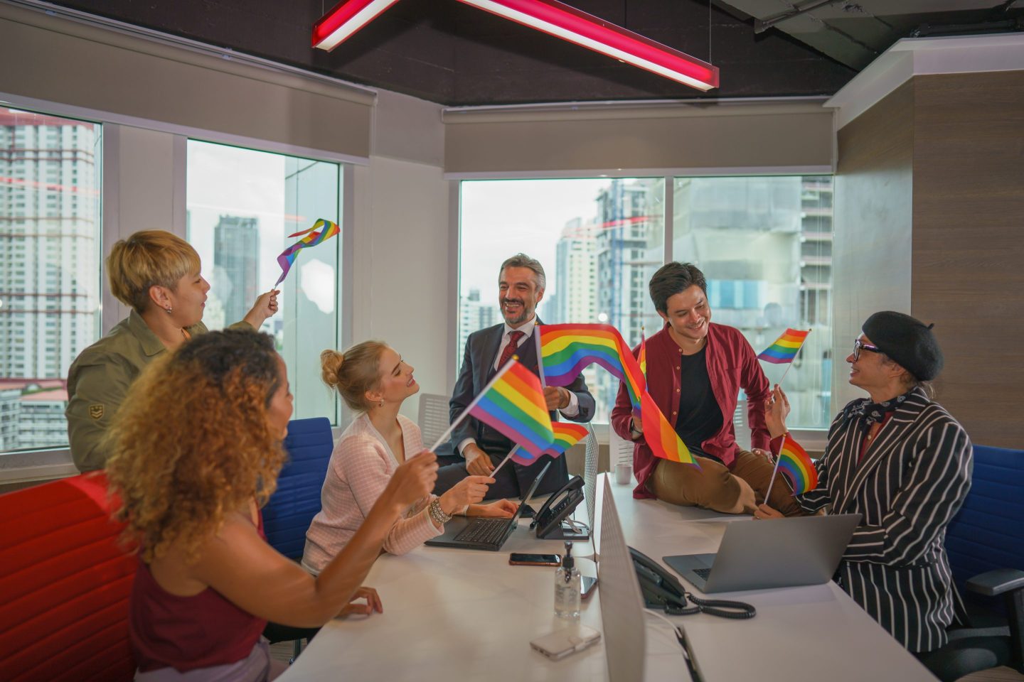 A group of colleagues sitting in an office holding LGBTQ Pride flags.