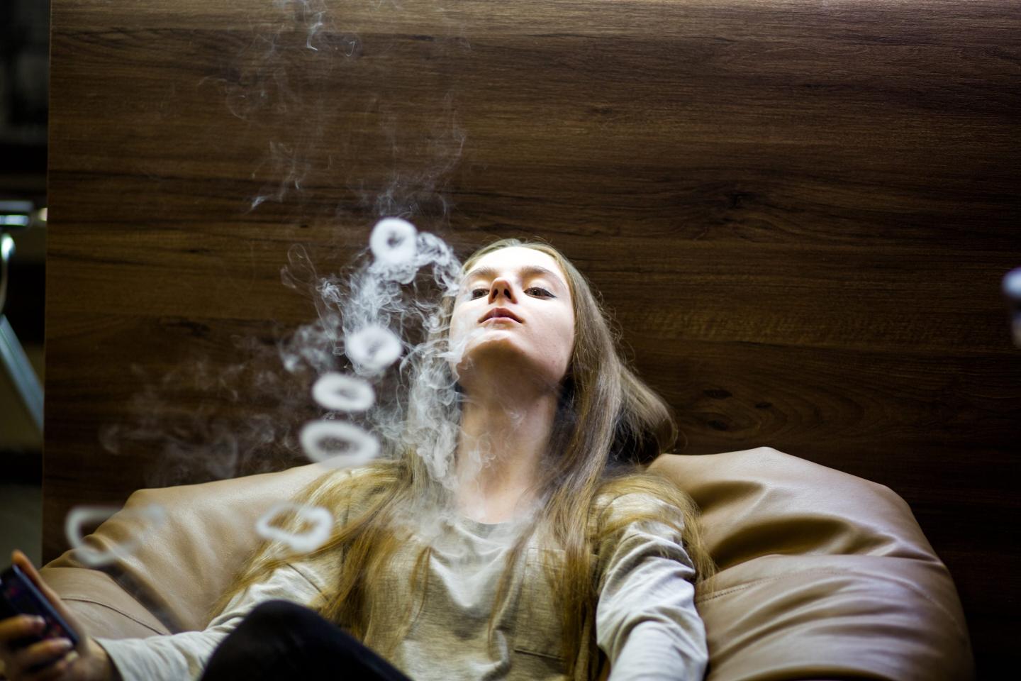Vaping teenager. Young pretty white caucasian teenage girl with problem skin smoking an electronic cigarette indoors.