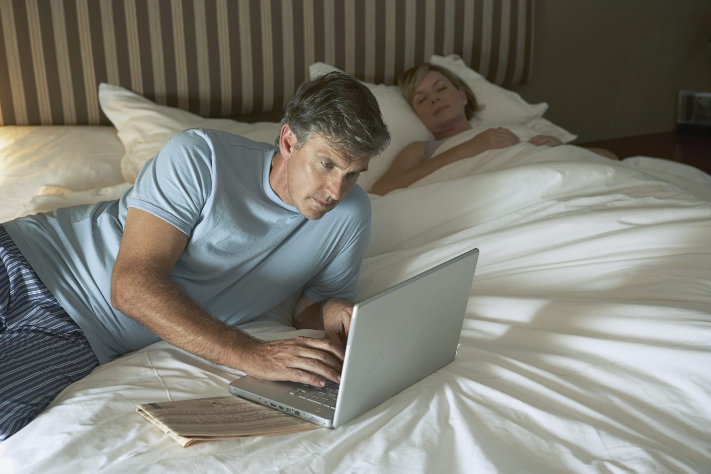Man using laptop in bed with wife sleeping