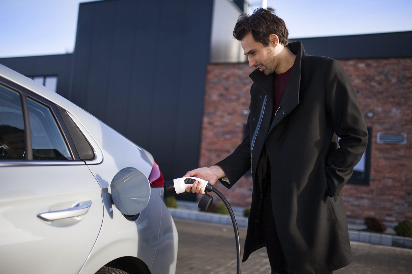 A man in a black jacket plugs a charger into an electric car