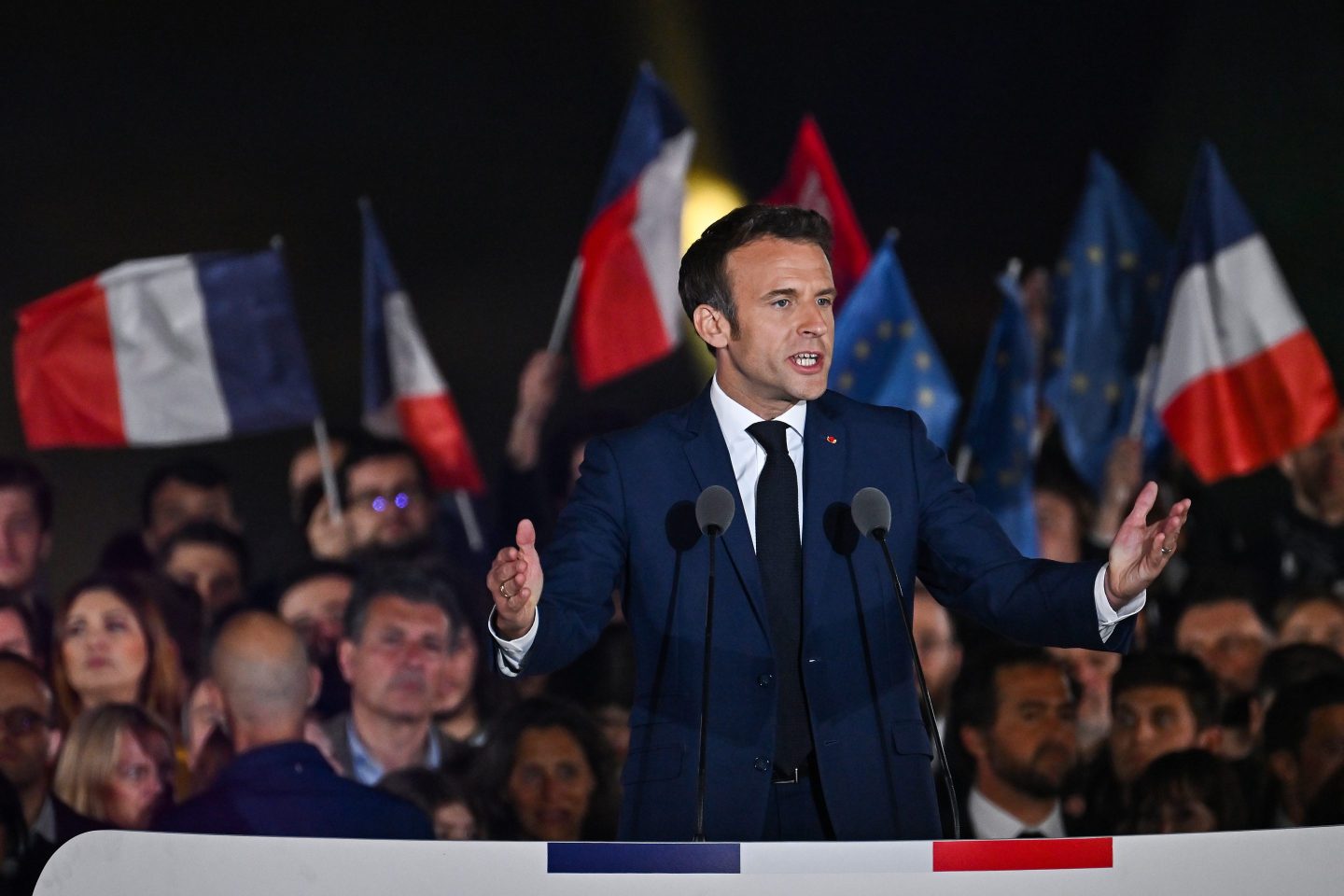 Emmanuel Macron talking on a podium with French flags behind him
