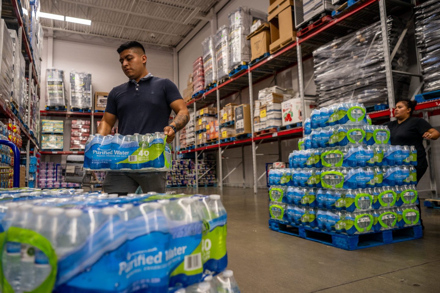 A young man is lifting a flat of water bottles from a large pile.