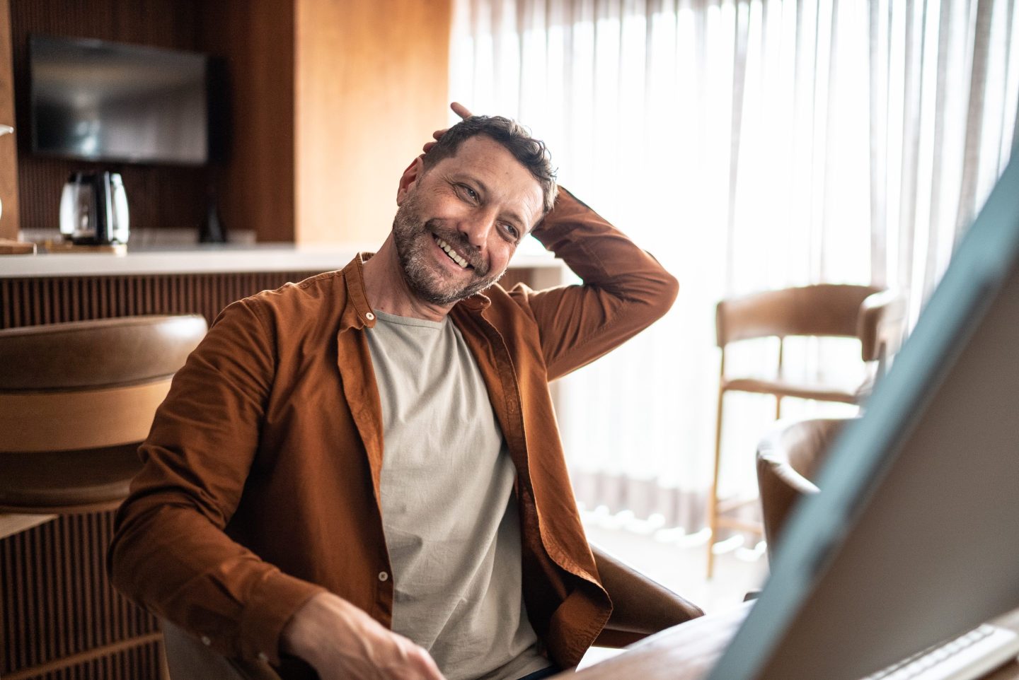 A man smiles while stretches while sitting in front of a computer screen.