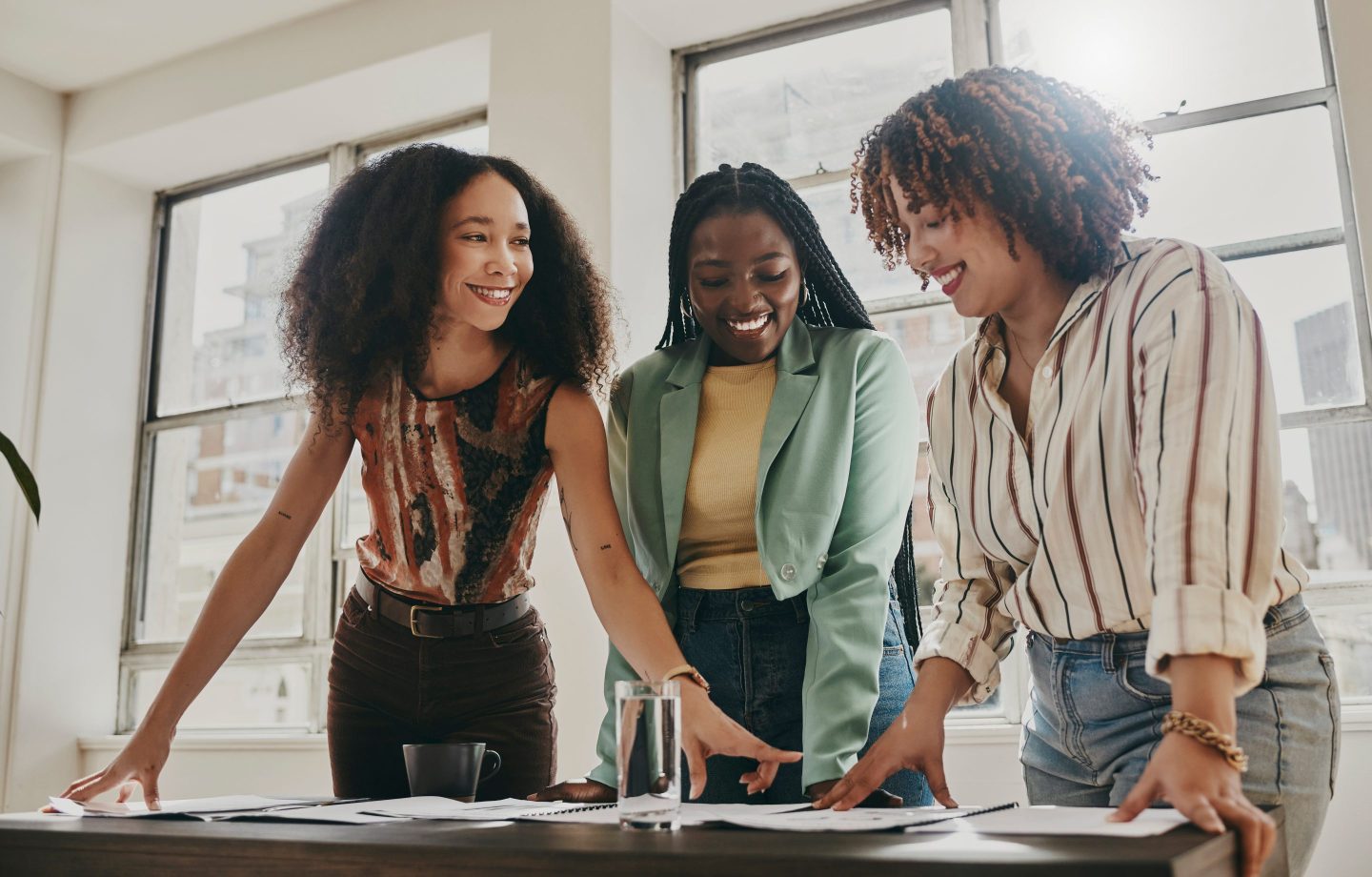 Three Black women look over documents, appearing to collaborate.